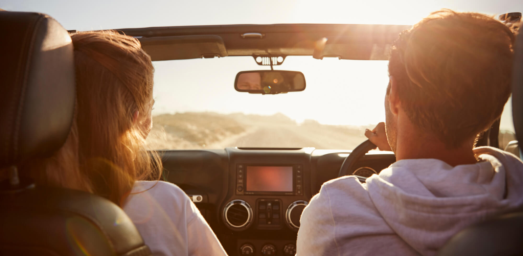 young couple driving with sunroof open rear passenger view 